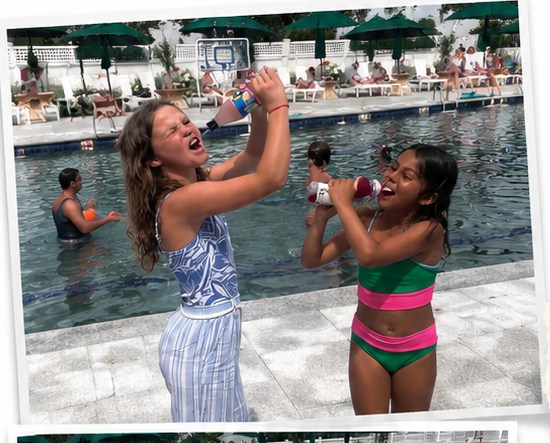 Two girls at the pool spraying water from bottles